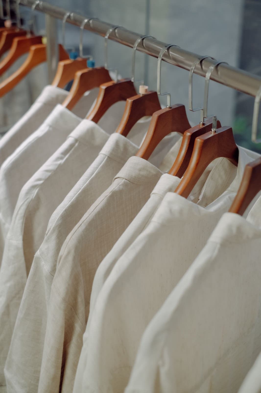 A rail of undyed linen shirts on wooden hangers